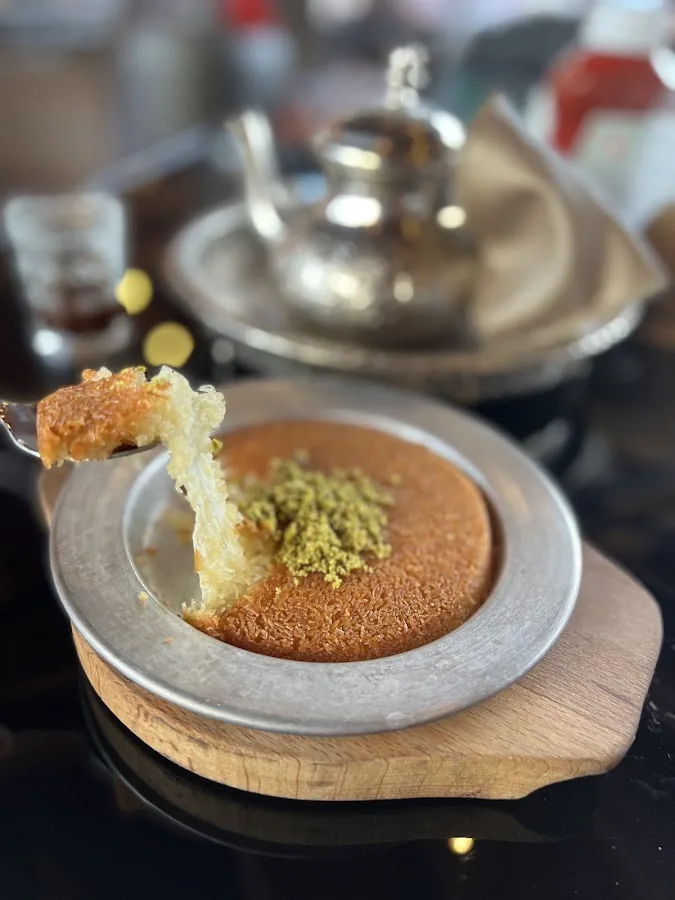 Knafeh in the pan with a molten cheese pull and crushed pistachios