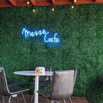 Mezze Cafe neon sign on the boxwood wall above a bistro table